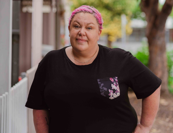 A woman with pink hair smiles at the camera.